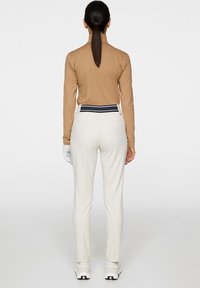 Jasno brązowa bluzka z długim rękawem o subtelnym wzorze, kremowe spodnie z czarno-białym paskiem w talii oraz białe buty sportowe.