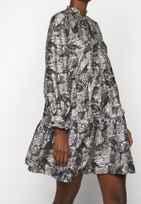 Kortärmad klänning med hög krage, som har ett virvlande mönster i grått och vitt, volang i nederkant och rynkad detalj vid midjan.