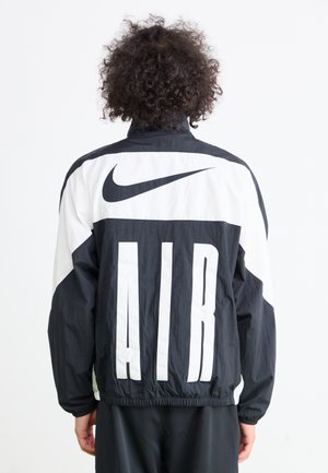 Black and white Nike jacket featuring large "AIR" lettering, a high collar, elastic cuffs, and a lightweight, textured fabric.