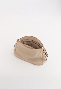 Beżowa torebka ze skórzanym teksturowanym wykończeniem o zakrzywionym kształcie, z złotym zamkiem błyskawicznym i uchwytami. Wnętrze zawiera małą kieszeń do organizacji.