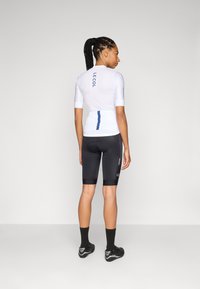 White cycling jersey with blue accents, short sleeves, and logo on the back, paired with black compressive shorts and black socks.
