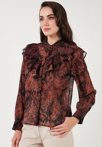 Sheer black blouse with red paisley patterns, ruffled collar, and button closure. Features long sleeves and delicate fabric texture.