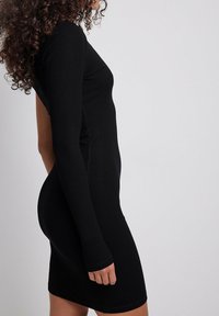Robe noire à côtes avec manches longues, design ajusté et découpe sur le côté. Texture lisse et silhouette jusqu'au genou.
