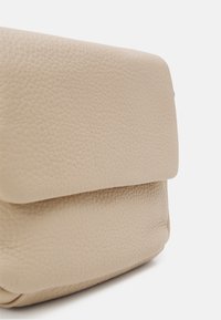 Beige läderväska med en strukturerad yta, som har en rundad spänne. Vinkeln betonar det mjuka materialet och den subtila sömmen.