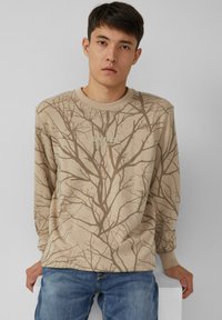 Felpa beige con stampa di rami, collo a coste e maniche lunghe. Notevole grafica "Solver" sul petto. Indossata con jeans blu.