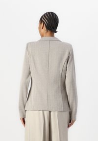 Maßgeschneiderter Hahnentritt-Blazer in Hellgrau und Beige, mit strukturierter Silhouette, Reverskragen und langen Ärmeln. Texturierte Oberfläche.
