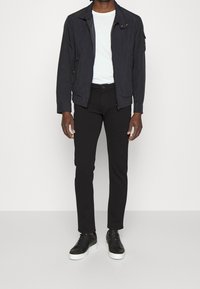 Svart zip-jacka med ståkrage, vit t-shirt, åtsittande svarta byxor och svarta sneakers med vita sulor.