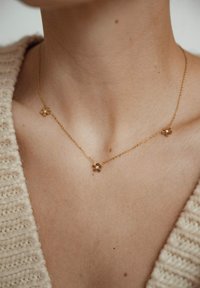 Collana d'oro con tre accenti a forma di fiore, caratterizzata da una delicata catena e piccole gemme al centro di ogni fiore.