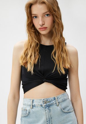 Czarny prążkowany top w stylu crop z przekręconym przodem, w połączeniu z jasnoniebieskimi szortami z wysokim stanem, które mają zapięcie na guzik i kieszenie.