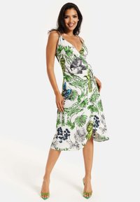 Floral print dress featuring a deep V-neck, thin straps, and a wrap design. Colors include white, green, blue, and black. Smooth, lightweight fabric.