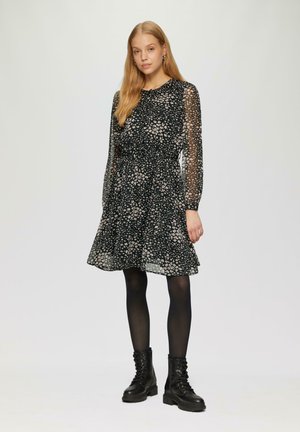 Robe noire à imprimé floral avec des manches longues transparentes, taille cintrée et ourlet évasé. Associée à des bottes de combat noires à lacets.