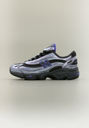 Baskets basses New Balance en argent métallisé et noir avec des accents violets, panneaux en mesh et semelle noire épaisse, vues de côté.