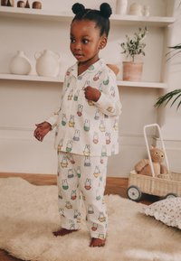 Ensemble de pyjama en coton blanc avec des imprimés de lapins colorés. Le haut possède un col, et le pantalon est ample avec une taille élastique.