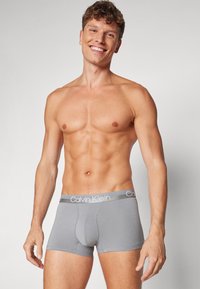 Pilki bokseriai su minkšta tekstūra, turintys plačią elastinę juostą, pažymėtą „Calvin Klein“ sidabro rašmenimis.