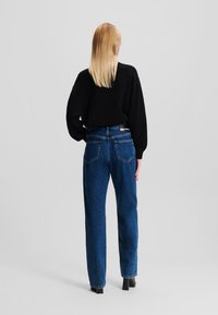 Črn pulover in svetlo modri kavbojki z visokim pasom. Kavbojke imajo ravno krojenje, denim teksturo in zadnje žepe z detajli pri šivanju.