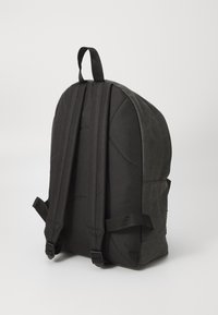 Schwarzer Rucksack mit gepolsterten Seiten, verstellbaren Trägern und einem oberen Tragegriff. Hat eine glatte Stoffstruktur und ein minimalistisches Design.