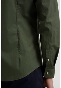 Långärmad skjorta i mörkgrön bomull med en böjd nederkant, med knäppning vid manschetterna och en subtil textur på tyget.