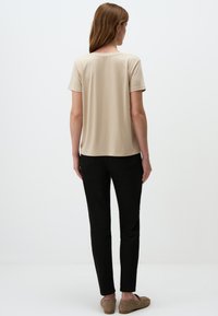 T-shirt beige a maniche corte con scollatura rotonda, texture liscia e una vestibilità rilassata, abbinato a pantaloni neri e scarpe marroni.