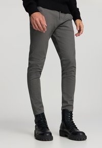 Pantaloni grigi aderenti con una superficie strutturata, caratterizzati da un design a vita bassa. Abbinati a stivali neri militari con lacci e a un maglione nero a coste.