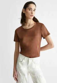 T-shirt corto a maniche corte in satin marrone con colletto rotondo, abbinato a pantaloni larghi di colore chiaro con tasche e accenti cuciti.