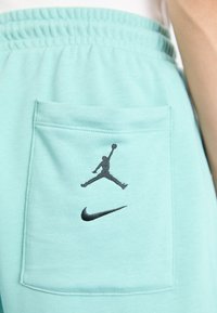 Világos teal színű, puha anyagú melegítőnadrág, fekete Jordan logó hímzéssel és Nike pipa mintával a hátsó zsebnél.