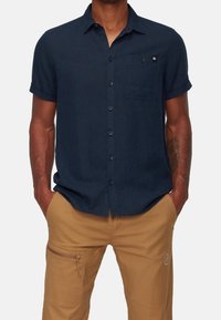 Camicia a maniche corte di colore blu navy, realizzata in tessuto testurizzato, con taschino sul petto e un piccolo logo ricamato sulla tasca.