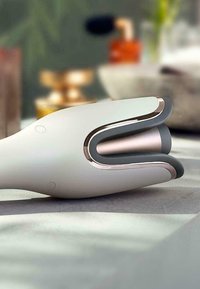 Handheld apparaat met een gladde witte behuizing, grijze accenten en een metallic roségouden rand. Heeft een gebogen, ergonomische vorm voor comfort.