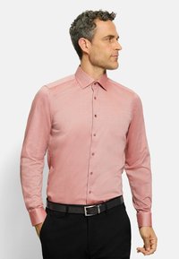Langärmliges Hemd mit Knopfleiste in Hellrot mit einem subtilen Karomuster, Kentkragen und passenden Knöpfen, kombiniert mit einem schwarzen Gürtel und Hose.