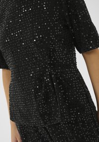 Top a maniche corte nera e pantaloni abbinati in tessuto testurizzato coperti di piccole paillettes nere indossati da una persona.