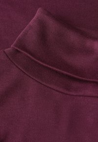 Bordeaux stof met een gevouwen kraag met een gladde textuur, die naadloos overgaat in het lichaam van het kledingstuk.