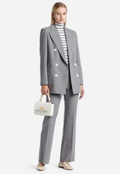 Gray tailored double-breasted blazer with large white buttons, paired with gray trousers, a striped turtleneck, and a white handbag.