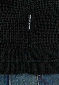 Černý pletený svetr s ribováním. Obsahuje malou tkanou etiketu s nápisem "JACK & JONES" v bílé barvě. Kombinováno s modrými džíny.
