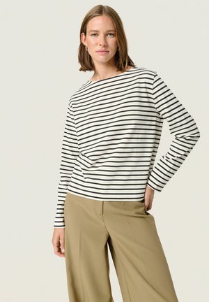 Cămașă cu mâneci lungi, în dungi alb-negru, din bumbac, cu un decolteu larg de tip bateau. Asortată cu pantaloni largi, cu talie înaltă, de culoare maro deschis.