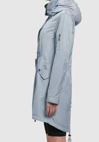 Veste bleu clair à manches longues avec capuche, fermeture éclair à l'avant, cordons réglables et poches latérales. Fabriquée en tissu lisse et résistant à l'eau.