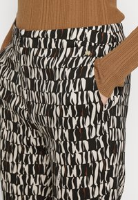 Zwarte broek met een wit en bruin abstract patroon, met een strak ontwerp, zijzakken en een knoopsluiting.