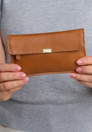 Hands with pink nails holding a brown leather wallet with a gold clasp in front of a gray sweater.