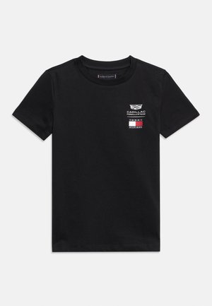 Melna t-krekls ar īsām piedurknēm un apaļu izgriezumu, ar maziem Cadillac Formula 1 Team un Tommy Hilfiger logotipiem uz kreisās krūtis augšējās daļas.