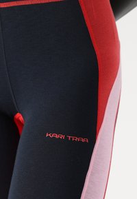 Navy polyester leggings with red and pink accents, featuring a textured waistband and logo "KARI TRAA" in red on the left thigh.