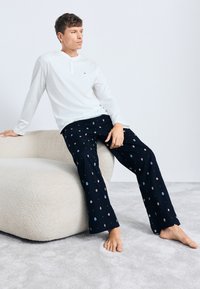 Chemise henley blanche à manches longues avec un col boutonné, associée à un pantalon de pyjama bleu marine orné d'un motif circulaire coloré.