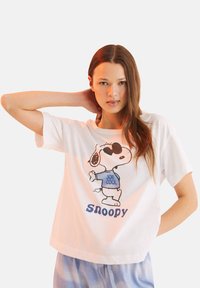 T-shirt bianca in cotone con Snoopy che indossa occhiali da sole e la scritta "JOE COOL". Maniche corte, vestibilità comoda, texture liscia, design giocoso.