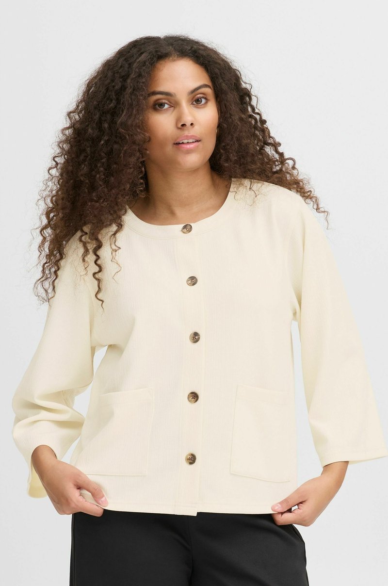 Chaqueta de botones color crema hecha de un tejido texturizado. Cuenta con un escote redondo, mangas de tres cuartos y dos bolsillos frontales.