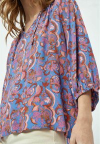 Blusa blue a maniche corte con un vivace motivo floreale in tonalità di rosa e ruggine, dal taglio rilassato e dettagli arricciati sulle maniche.