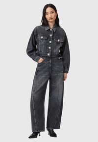 Chaqueta vaquera negra recortada con botones en forma de flor, combinada con jeans de pierna ancha de cintura alta. Textura suave con detalles de costura en contraste.