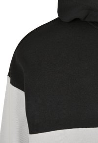 Hooded sweatshirt featuring a black top section and white bottom section, made of textured fabric with a relaxed fit.