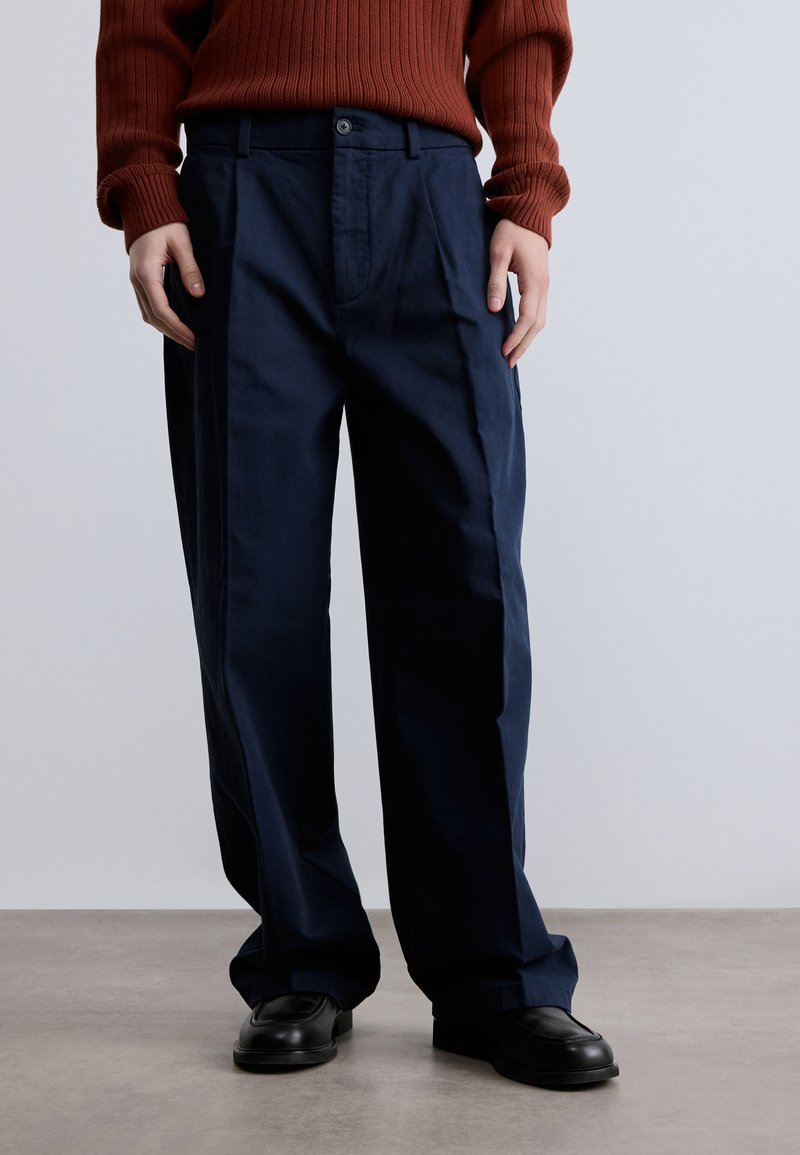 Σκούρο μπλε παντελόνια με ευθεία κοπή, που διαθέτει πτυχή μπροστά, δύο πλαϊνές τσέπες και κούμπωμα με κουμπί. Απαλή υφή υφάσματος.