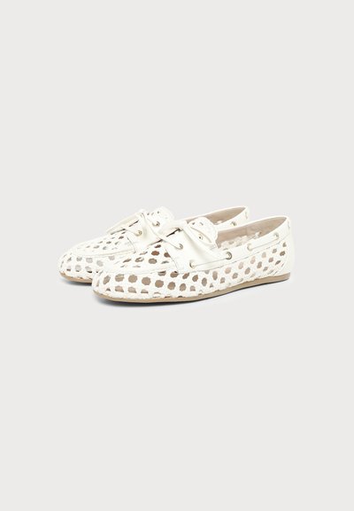 Paire de mocassins en cuir blanc avec un design ajouré hexagonal tissé et une fermeture à lacets sur un fond gris clair.
