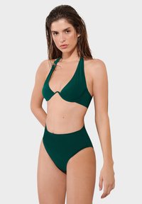 Zeleni bikini set sa halter topom i V-izrezom te visokim donjim dijelom. Izrađen od glatkog materijala s minimalnim šavovima.