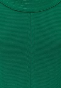 Grön strukturerad tyg med vertikal ribbad mönster och en central söm under en rund halsringning.