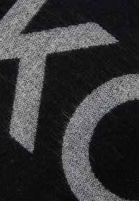 Černá tkanina s výrazným bílým grafickým designem. Textura vypadá tkaná s mírným chmířím, což dodává hloubku vizuálním prvkům.