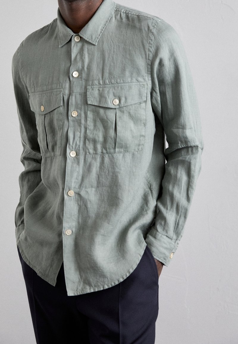 Hellgrünes Langarmhemd aus strukturiertem Stoff mit zwei aufgesetzten Taschen vorne und Knopfverschluss. Abgerundeter Saum und beige Knöpfe.